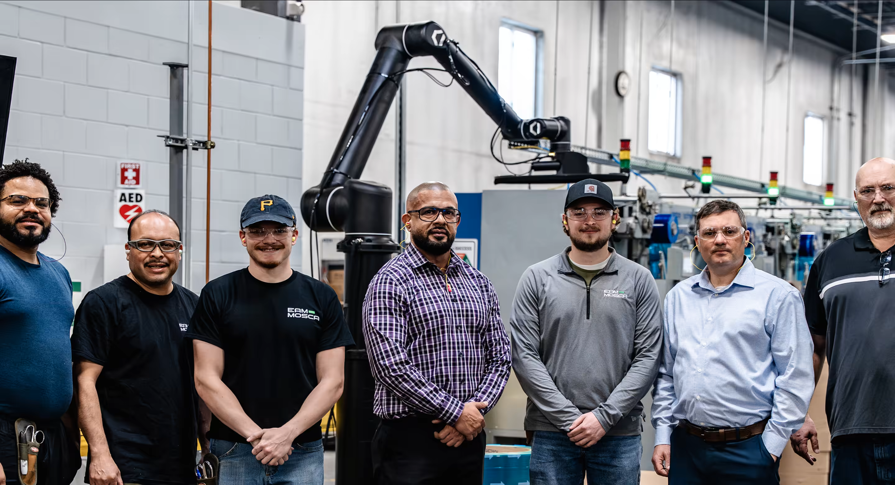 A shop-floor team standing in front of a Standard Bots robot arm in a manufacturing facility