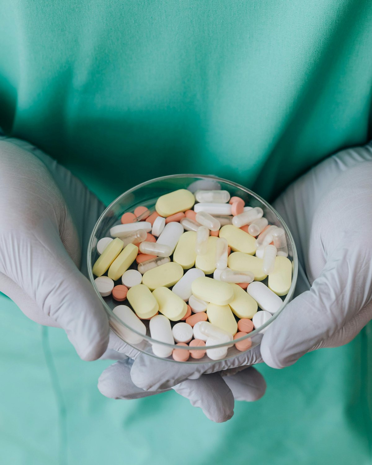 Gloved hands holding a glass dish of tablets and capsules