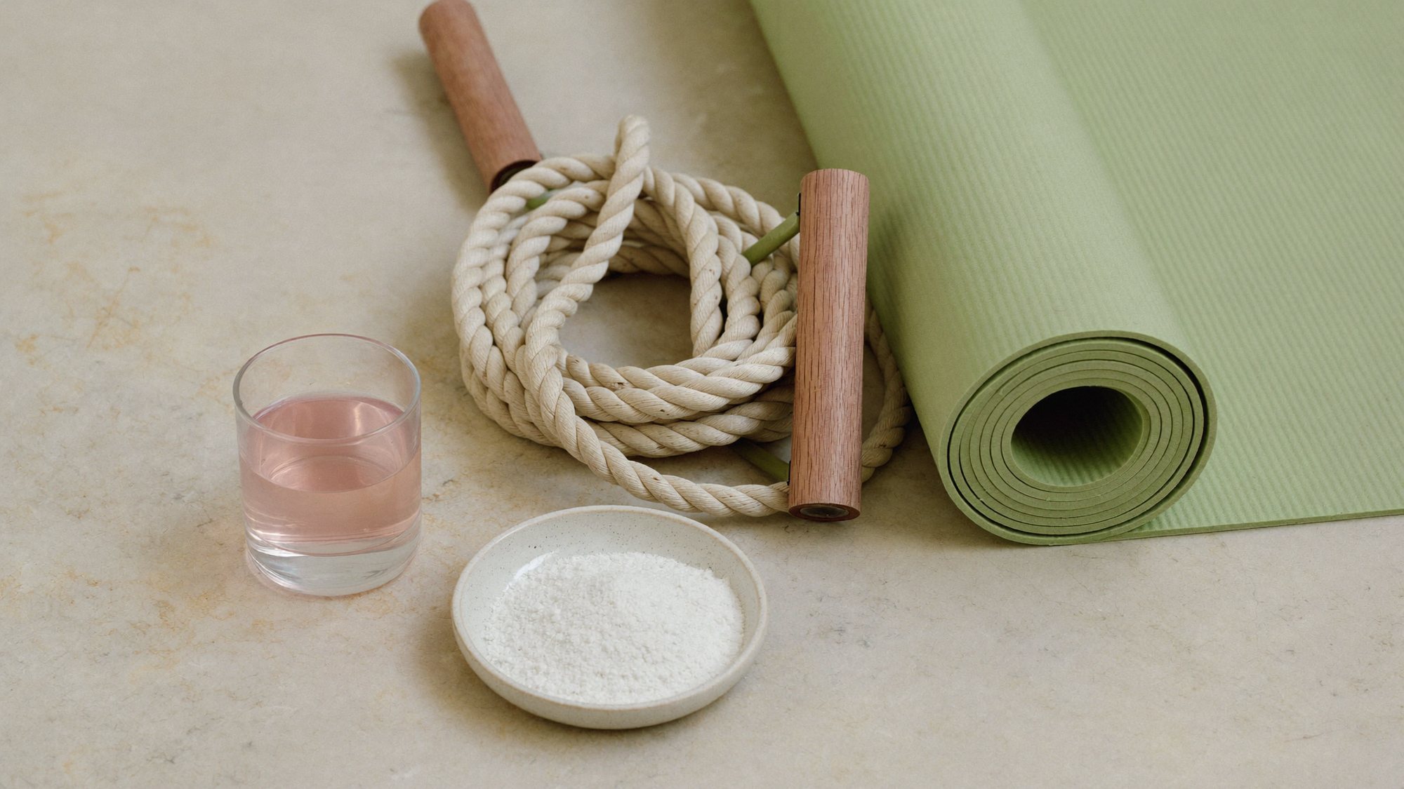 BCAA powder in a dish beside a pink drink, a skipping rope and a rolled yoga mat
