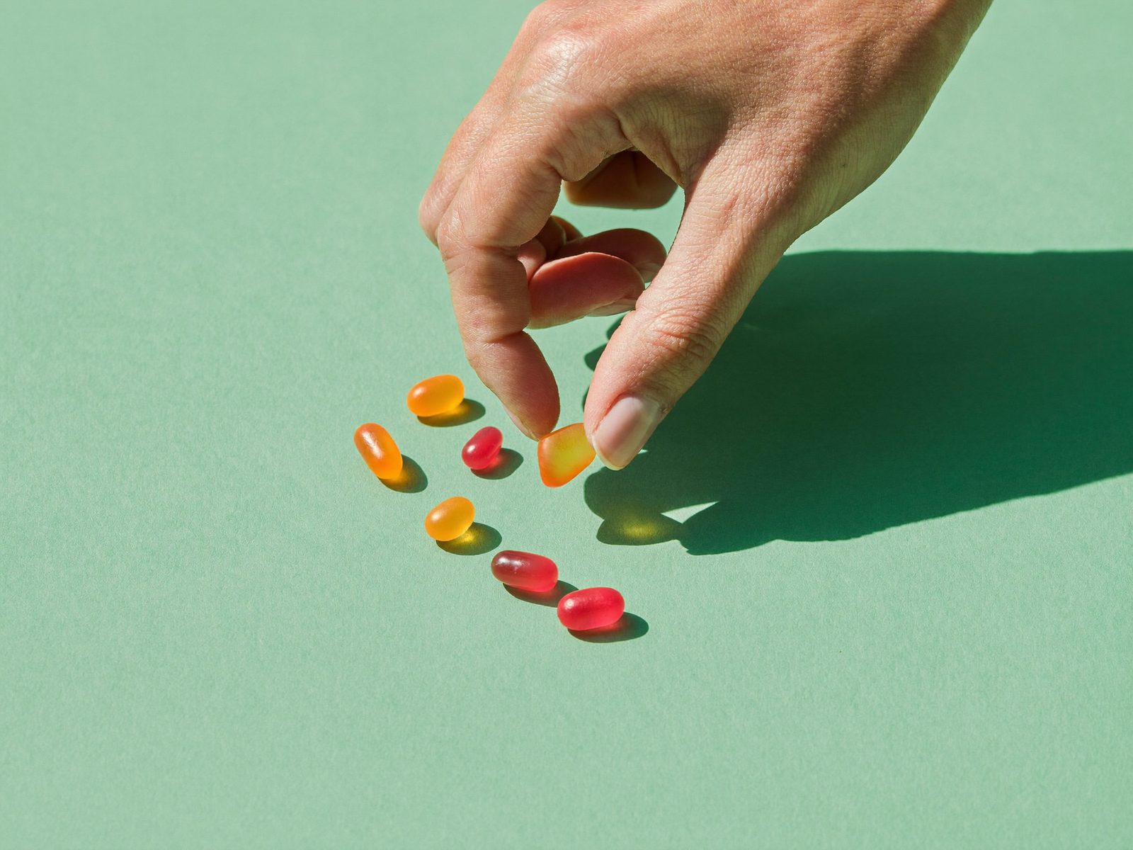 Hand picking an orange gummy from a pile of fruit gummies