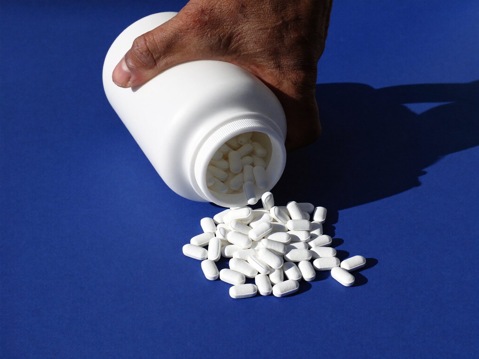 White oval tablets spilling from an unlabelled bottle onto a blue surface