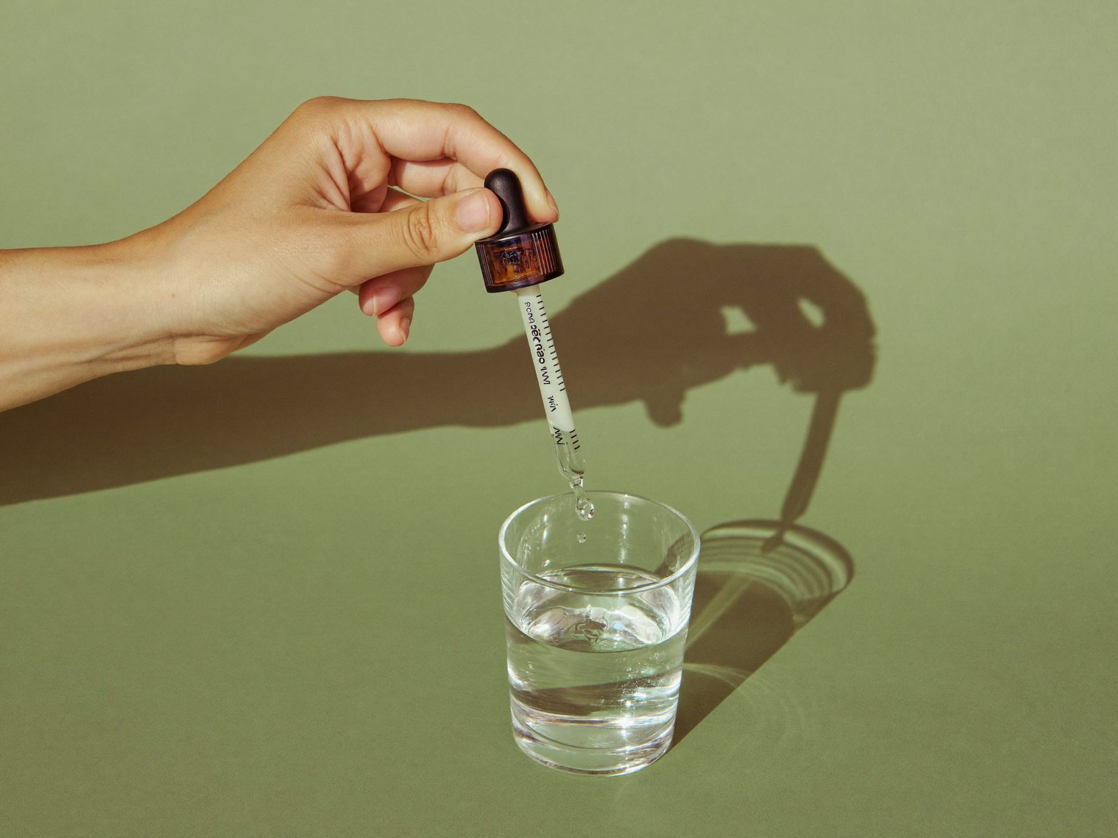 Hand squeezing a dropper of liquid supplement into a glass of water