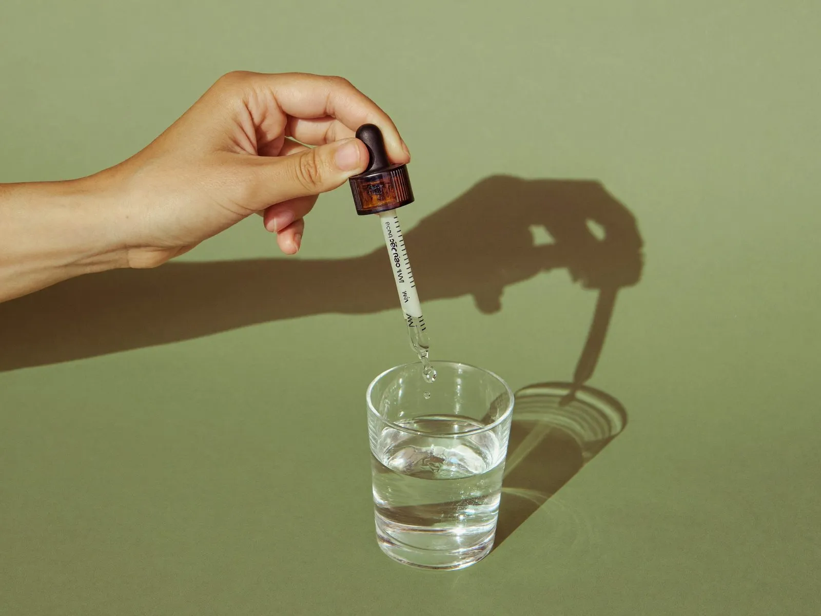Hand squeezing a dropper of liquid supplement into a glass of water