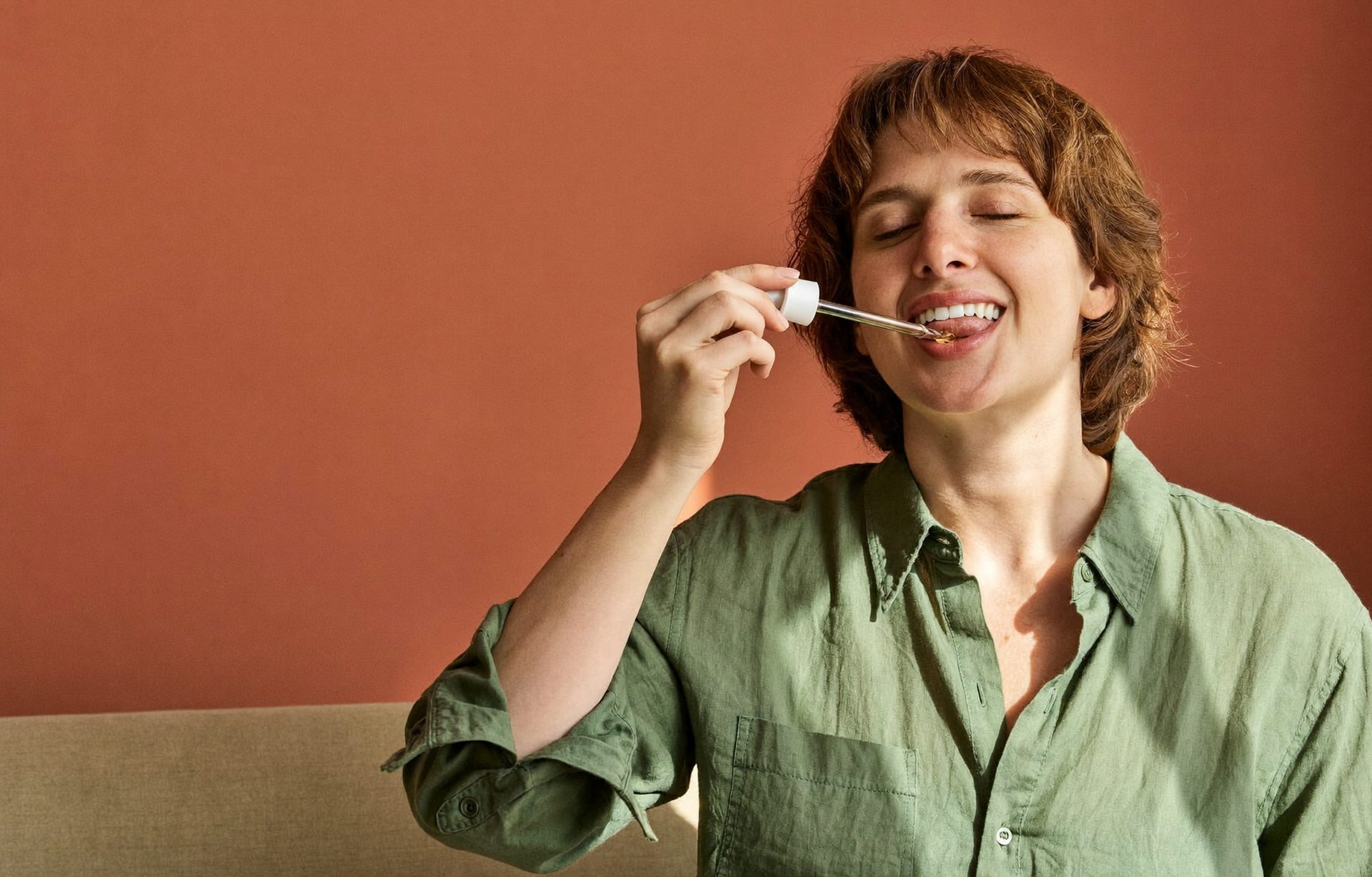 Woman in a linen shirt taking liquid supplement drops from a glass dropper
