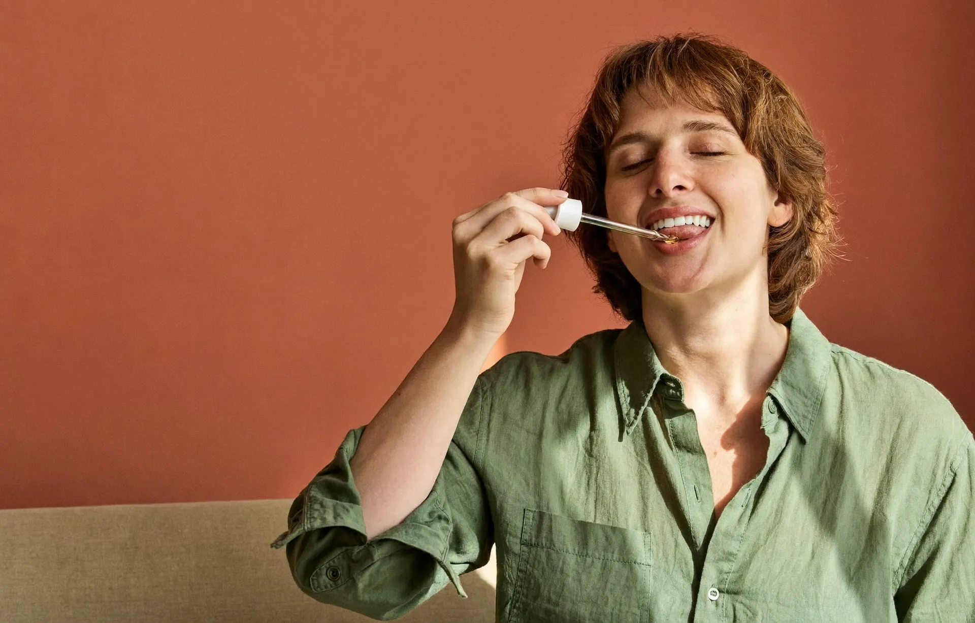 Woman in a linen shirt taking liquid supplement drops from a glass dropper