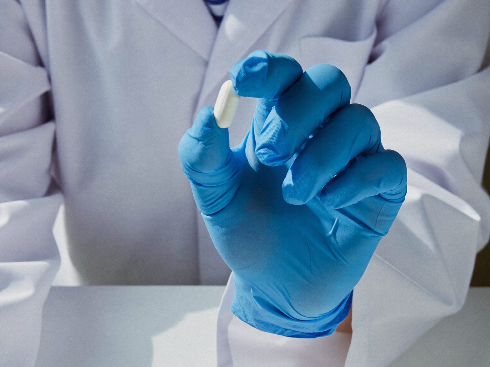 Technician holding a single tablet over a dish of tablets on a lab bench