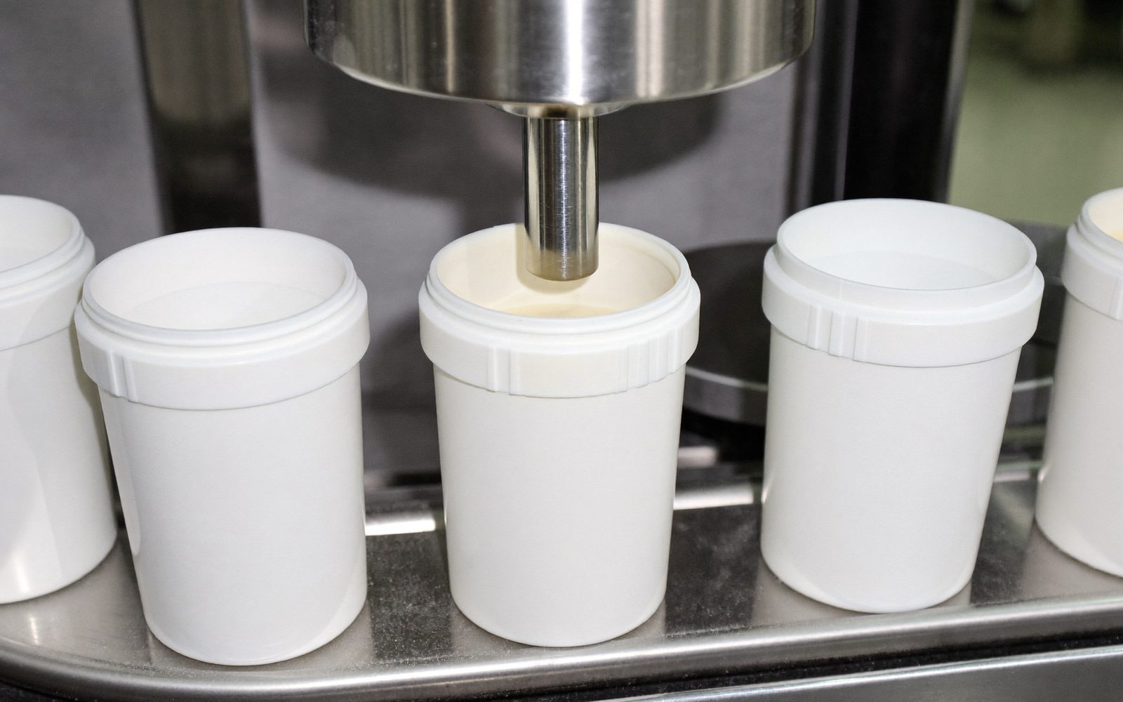 Plain white tubs on a filling line, one being dosed with powder from a stainless auger filler