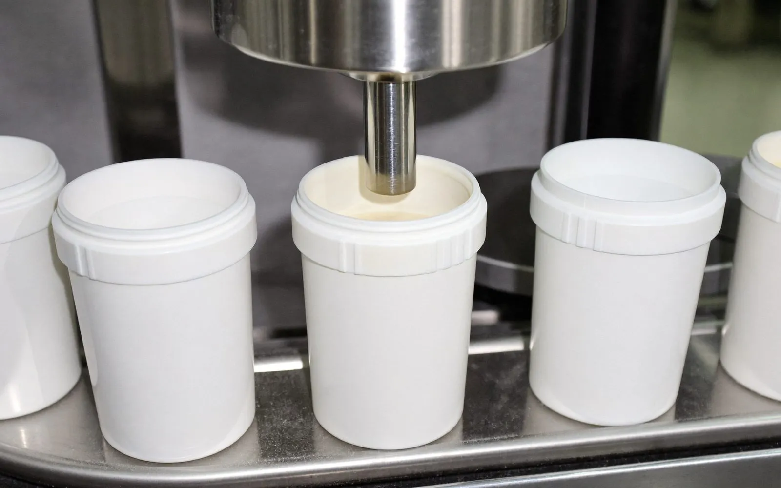Plain white tubs on a filling line, one being dosed with powder from a stainless auger filler