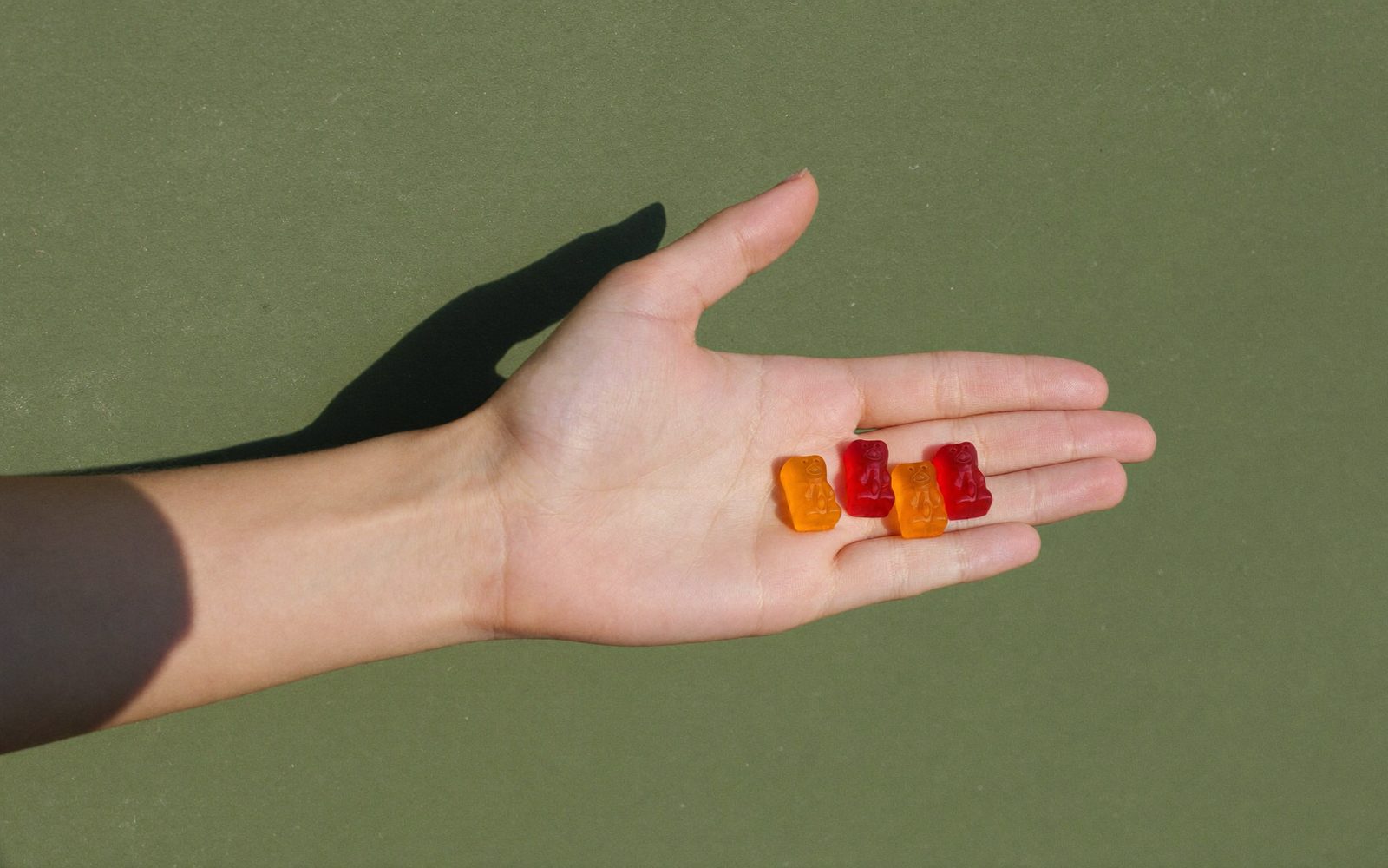 Open palm holding three small gummy bear supplements against a green wall