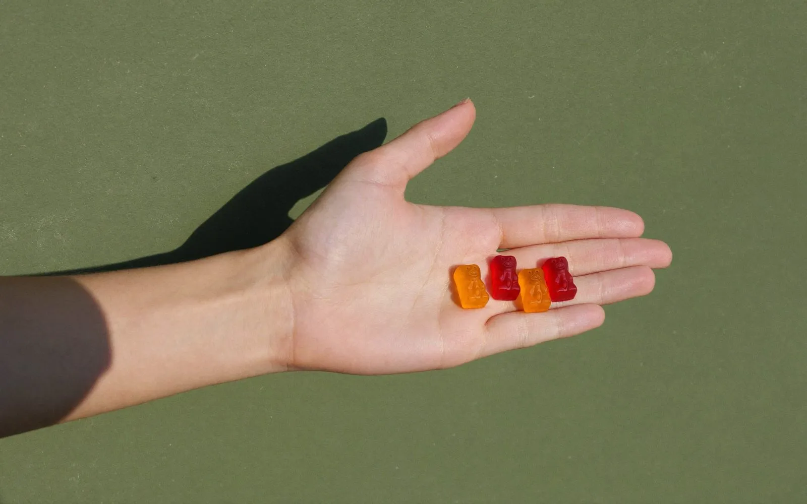 Open palm holding three small gummy bear supplements against a green wall