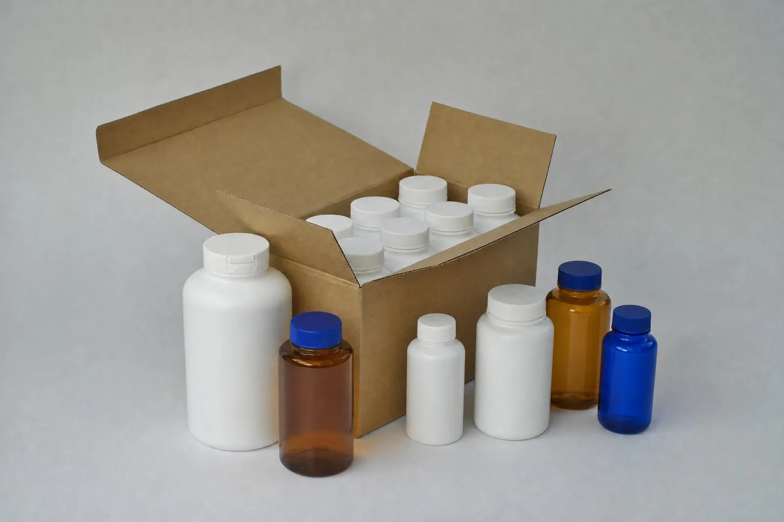 Unlabeled white, amber and cobalt HDPE and PET bottles beside a twelve-bottle shipping carton
