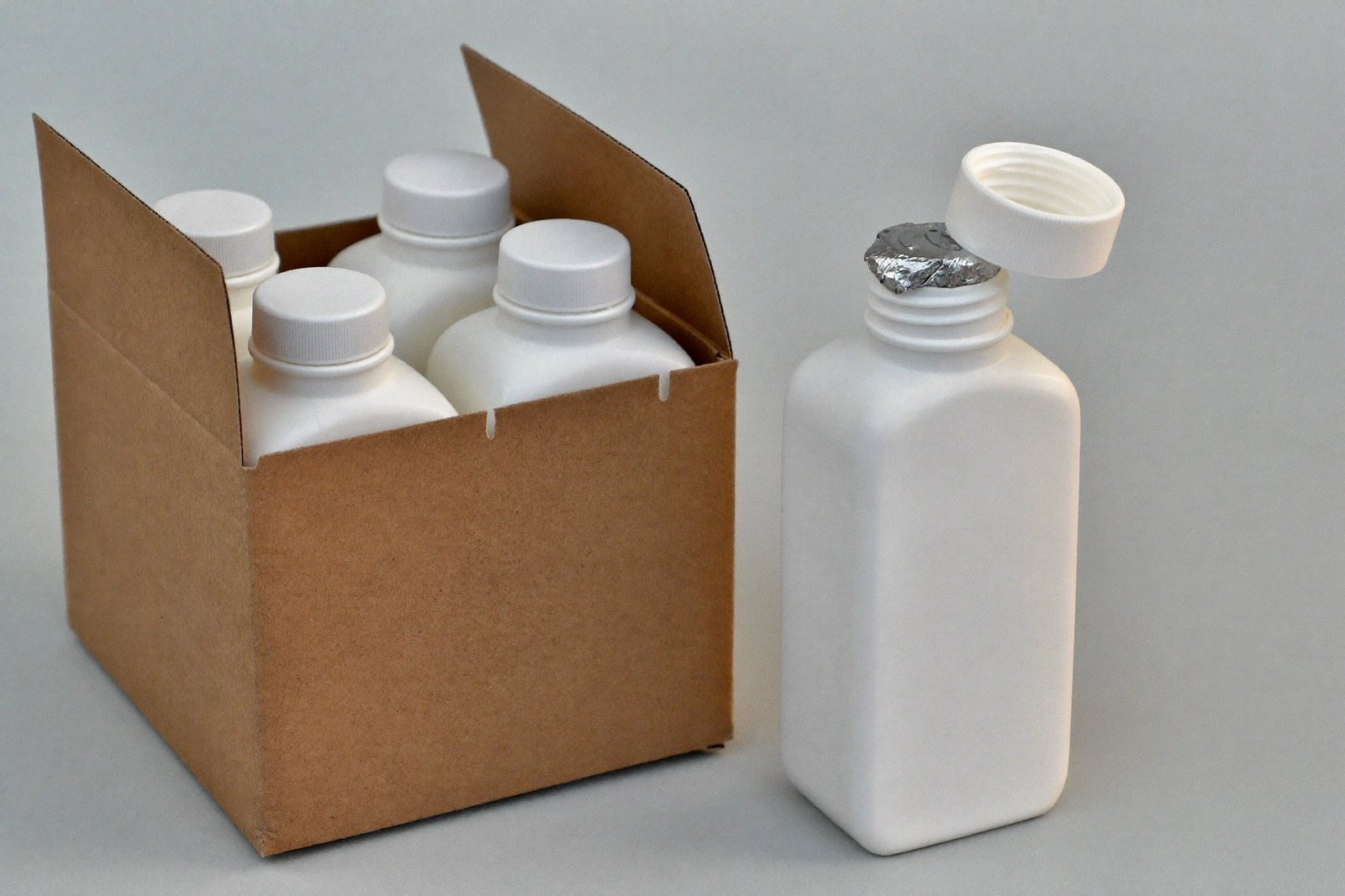 Foil induction seal on an open bottle beside a shipping carton