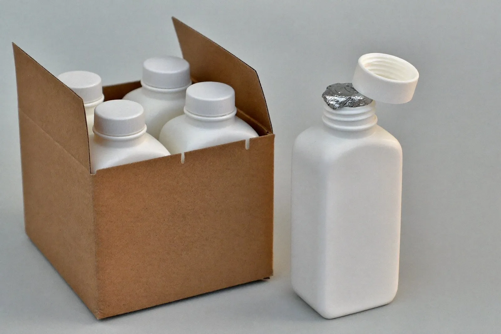 Foil induction seal on an open bottle beside a shipping carton