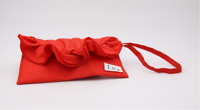 Red fabric clutch bag with ruffled opening and a matching strap, featuring a small white tag with text.