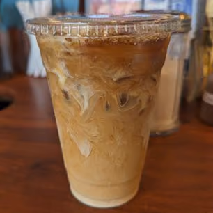 Close-up of iced coffee with cream in a clear plastic cup with a lid on a wooden table.