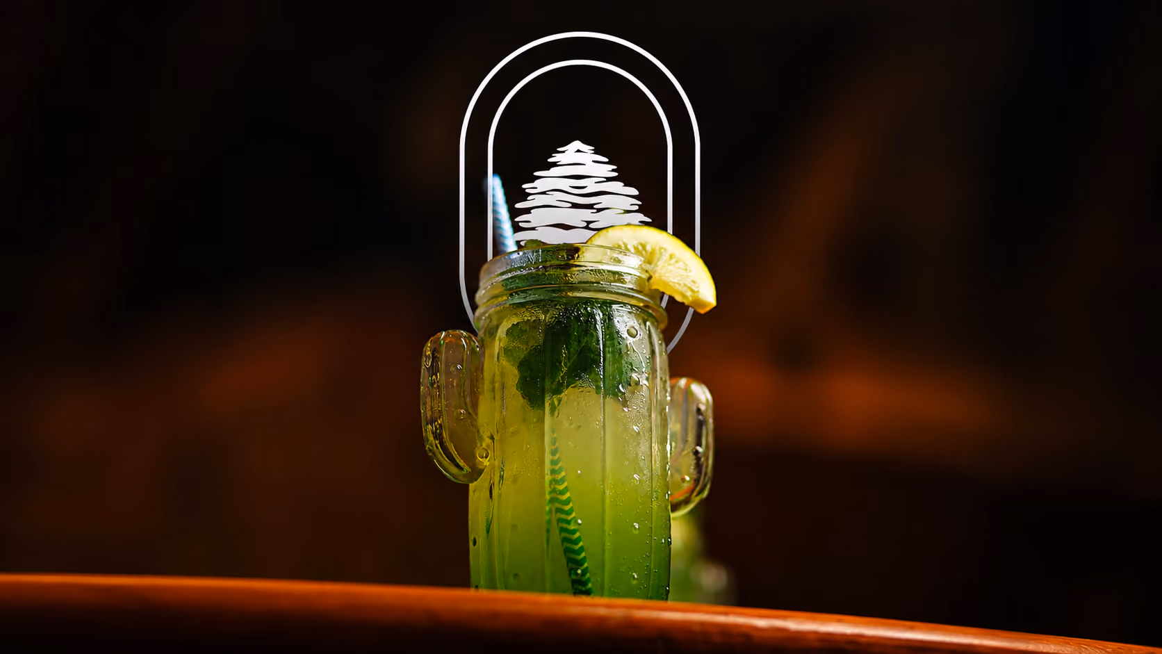 Green drink with mint and lemon slice in a cactus-shaped glass with a straw on wooden surface.