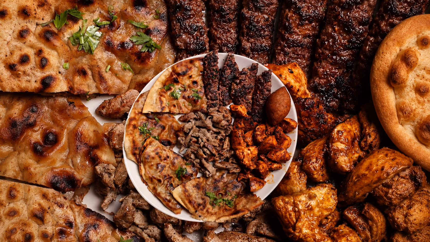 Plate with grilled meat, bread, and herbs surrounded by various grilled meats and flatbreads.