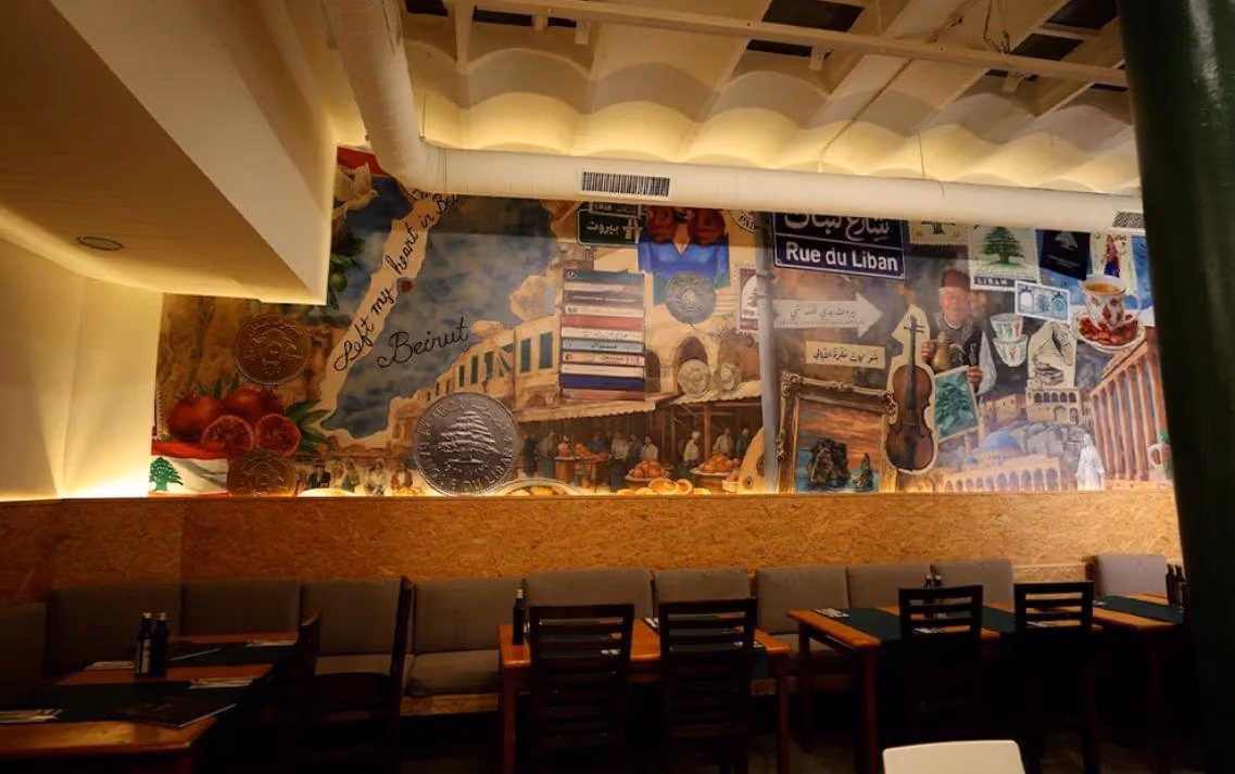 Interior of a restaurant with mural featuring Lebanese culture, coins, books, and a Beirut tram.