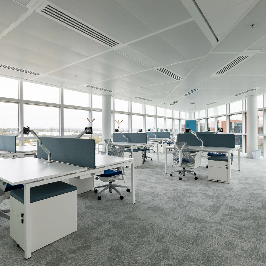 Bright open-plan office with white desks and ergonomic chairs by large windows