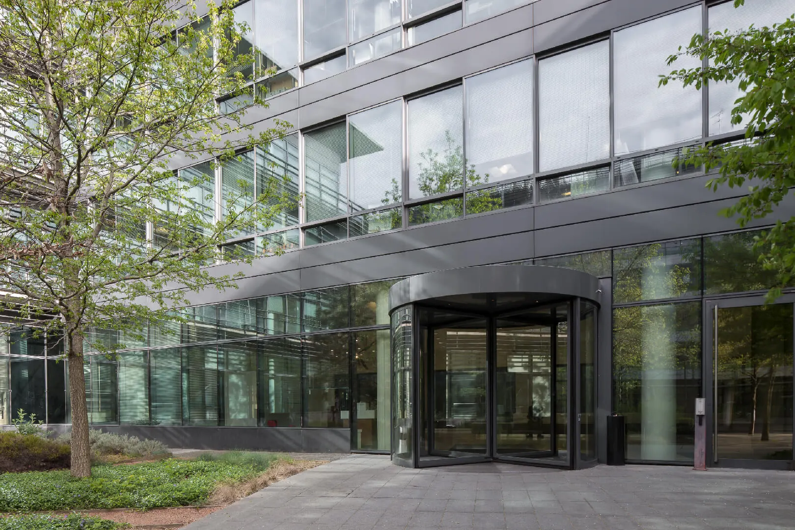 Office building entrance with revolving glass door surrounded by trees