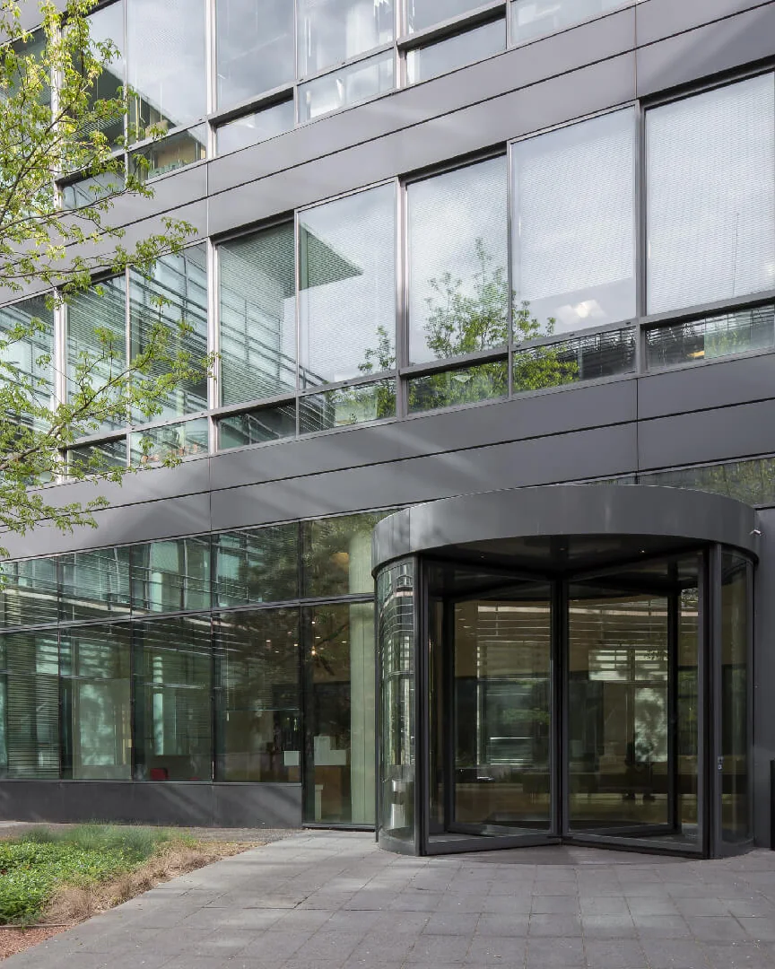 Office building entrance with revolving glass door surrounded by trees