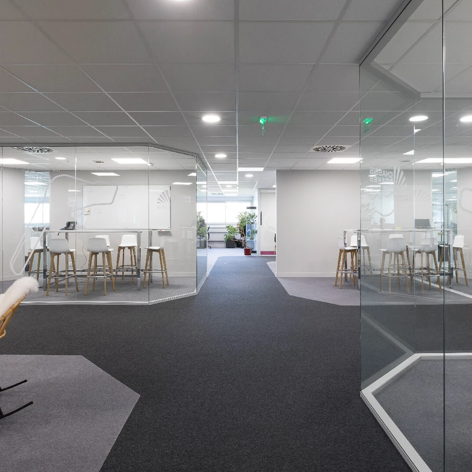 Glass-walled meeting rooms with high stools and a rocking chair on dark carpet