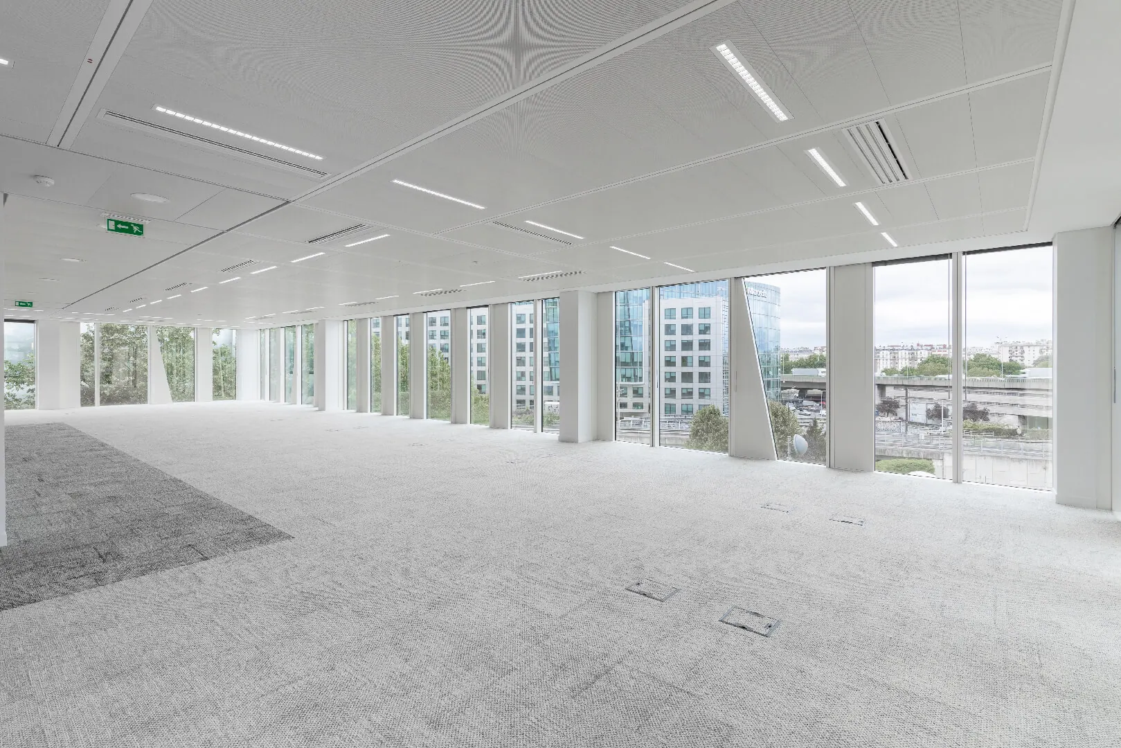 Empty open-plan office floor with grey carpet and floor-to-ceiling windows