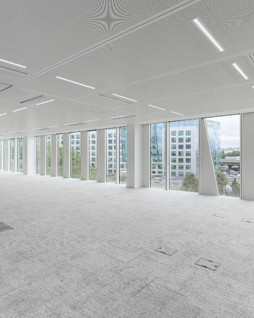 Empty open-plan office floor with grey carpet and floor-to-ceiling windows