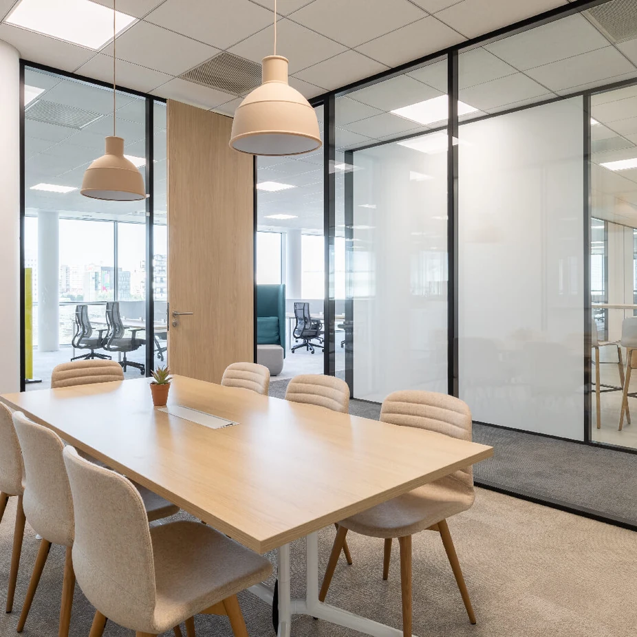 Meeting room with light wood table, upholstered chairs and black-framed glass walls
