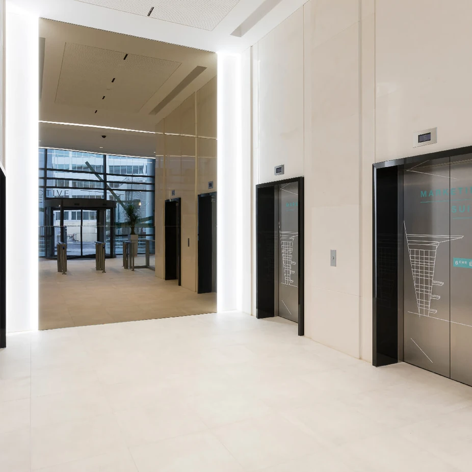 Bright lift lobby with black-framed elevator doors and cream stone walls