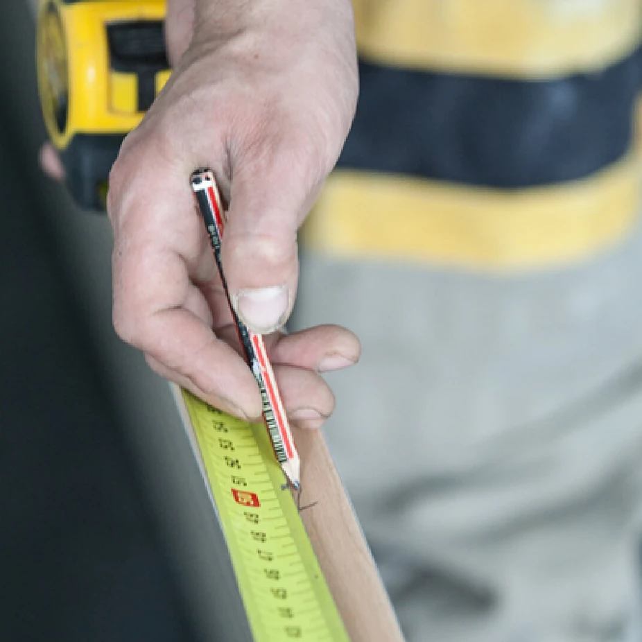 Worker marking a wooden batten with a pencil and tape measure