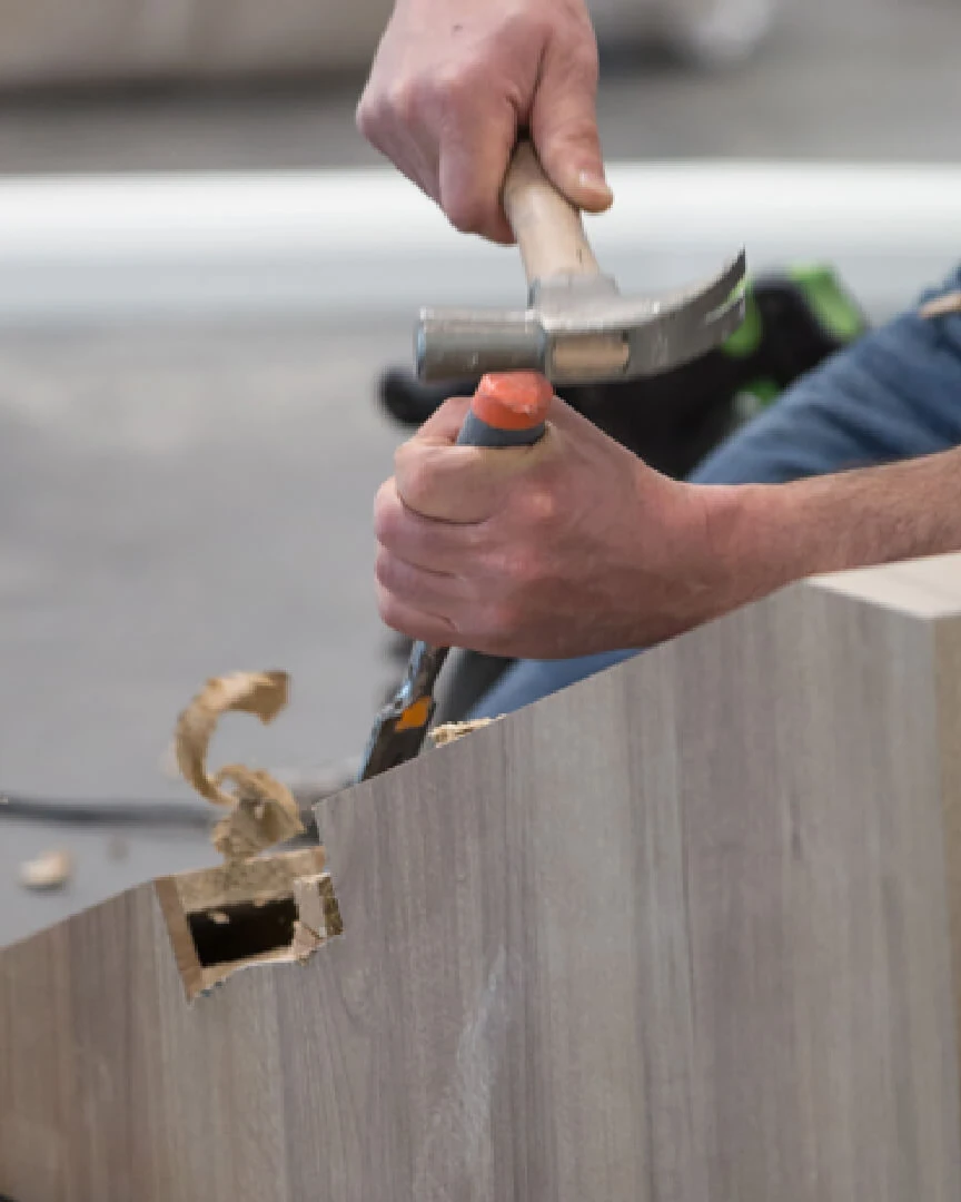 Carpenter hammering a fitting into a wood laminate panel