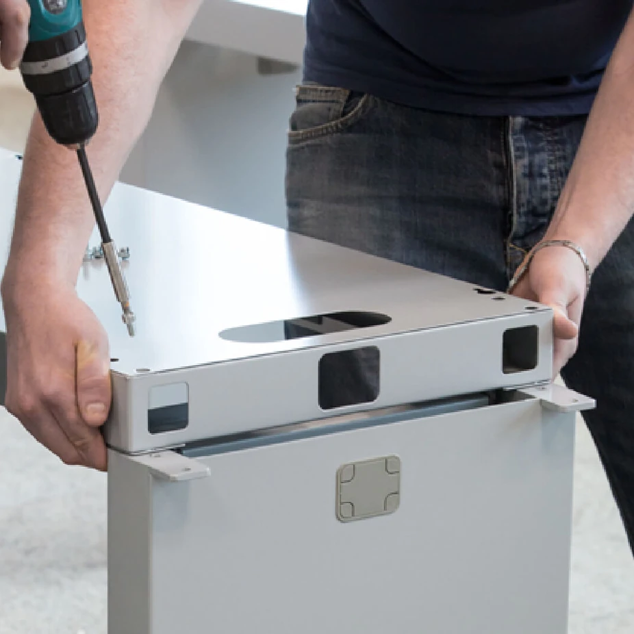 Installer assembling a white metal desk unit with a cordless drill