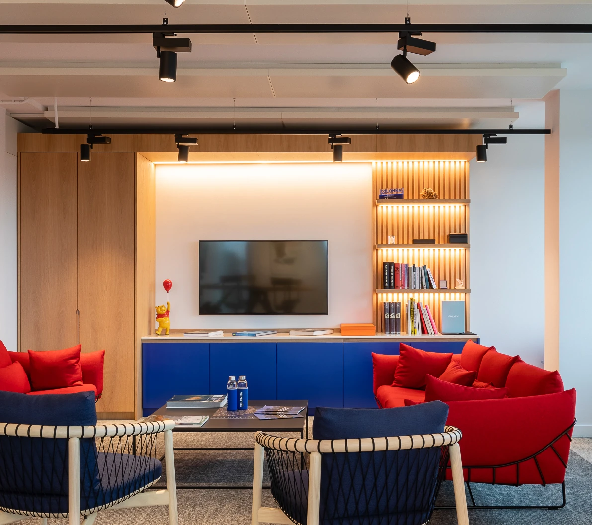 Office lounge with red and navy armchairs, blue cabinet and backlit wooden shelving