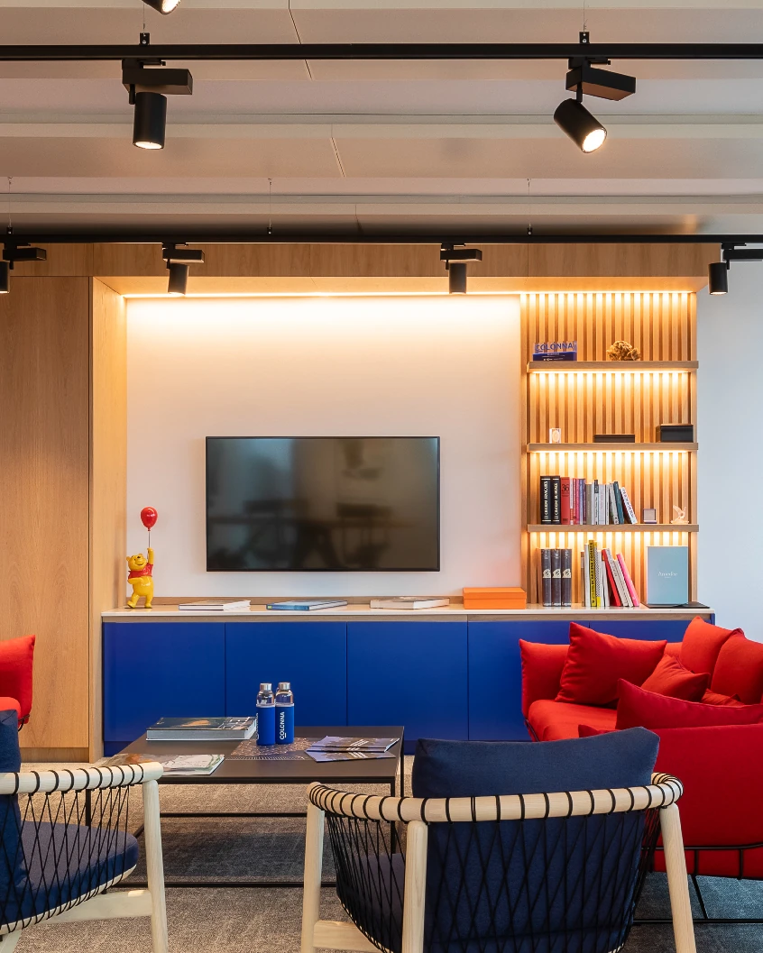 Office lounge with red and navy armchairs, blue cabinet and backlit wooden shelving