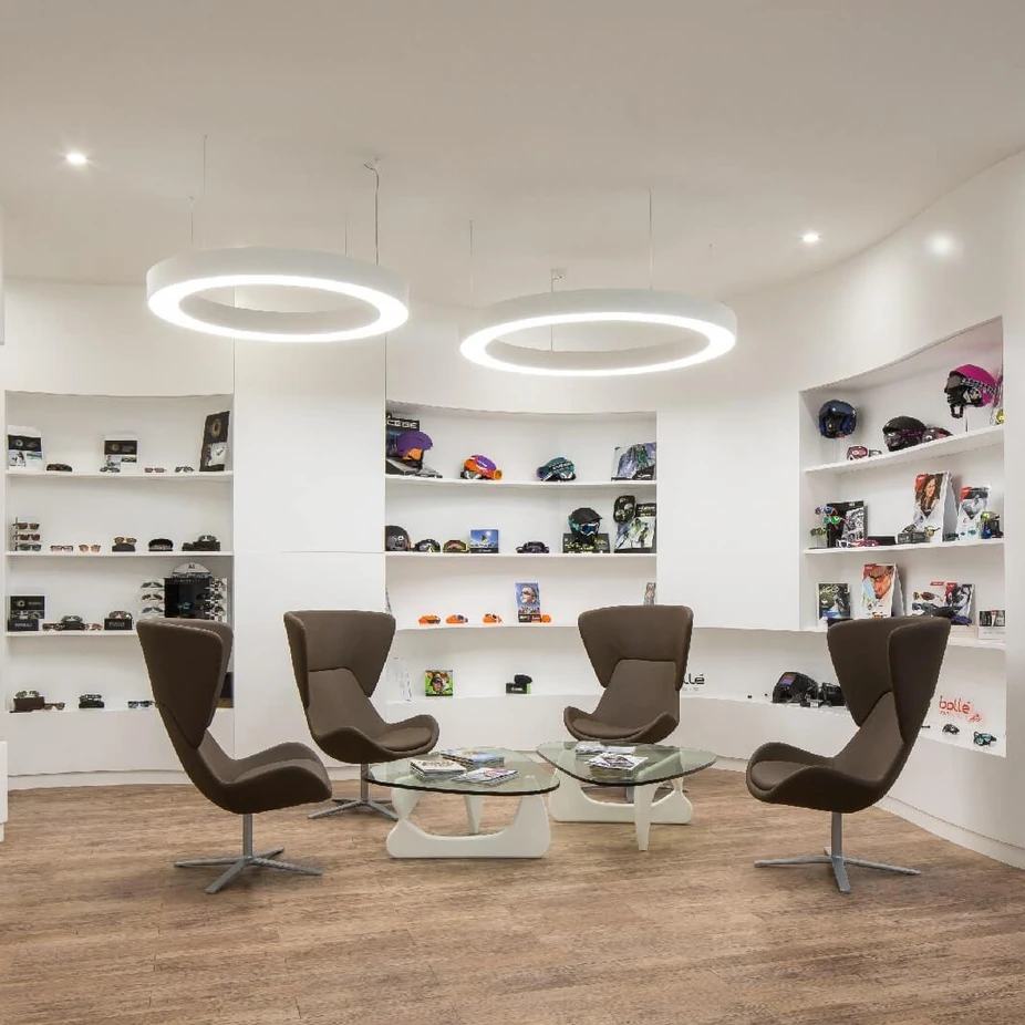 Curved white showroom with product shelves, brown swivel armchairs and ring ceiling lights