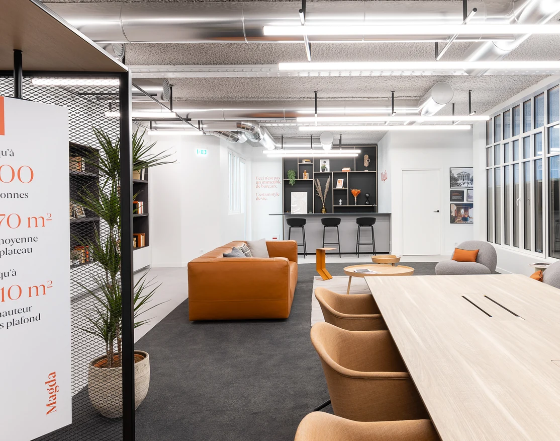 Bright meeting room with a long light-wood table, orange chairs and a large plant