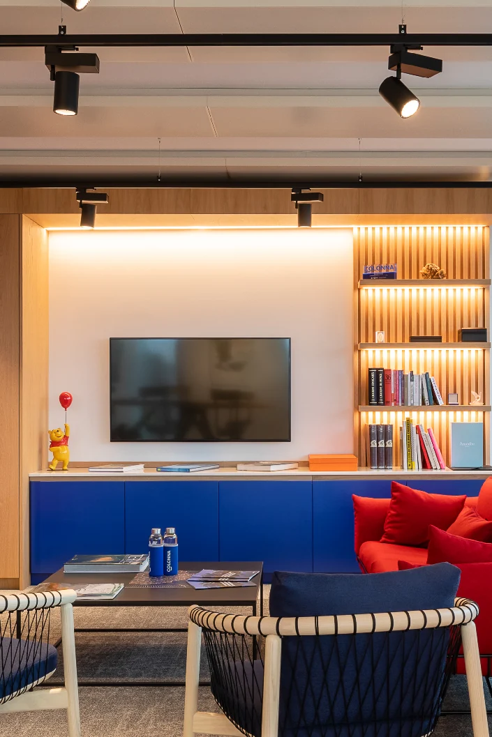 Lounge corner with red and navy armchairs, blue sideboard and backlit wooden shelving