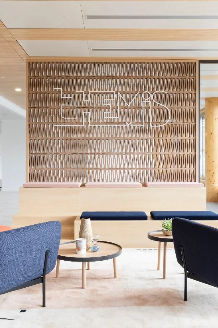 Reception lounge with navy armchairs in front of a perforated wooden feature wall