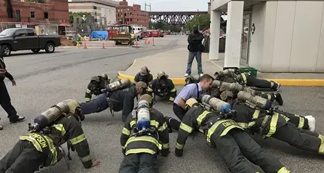 Firefighters in full gear resting on ground during training exercise