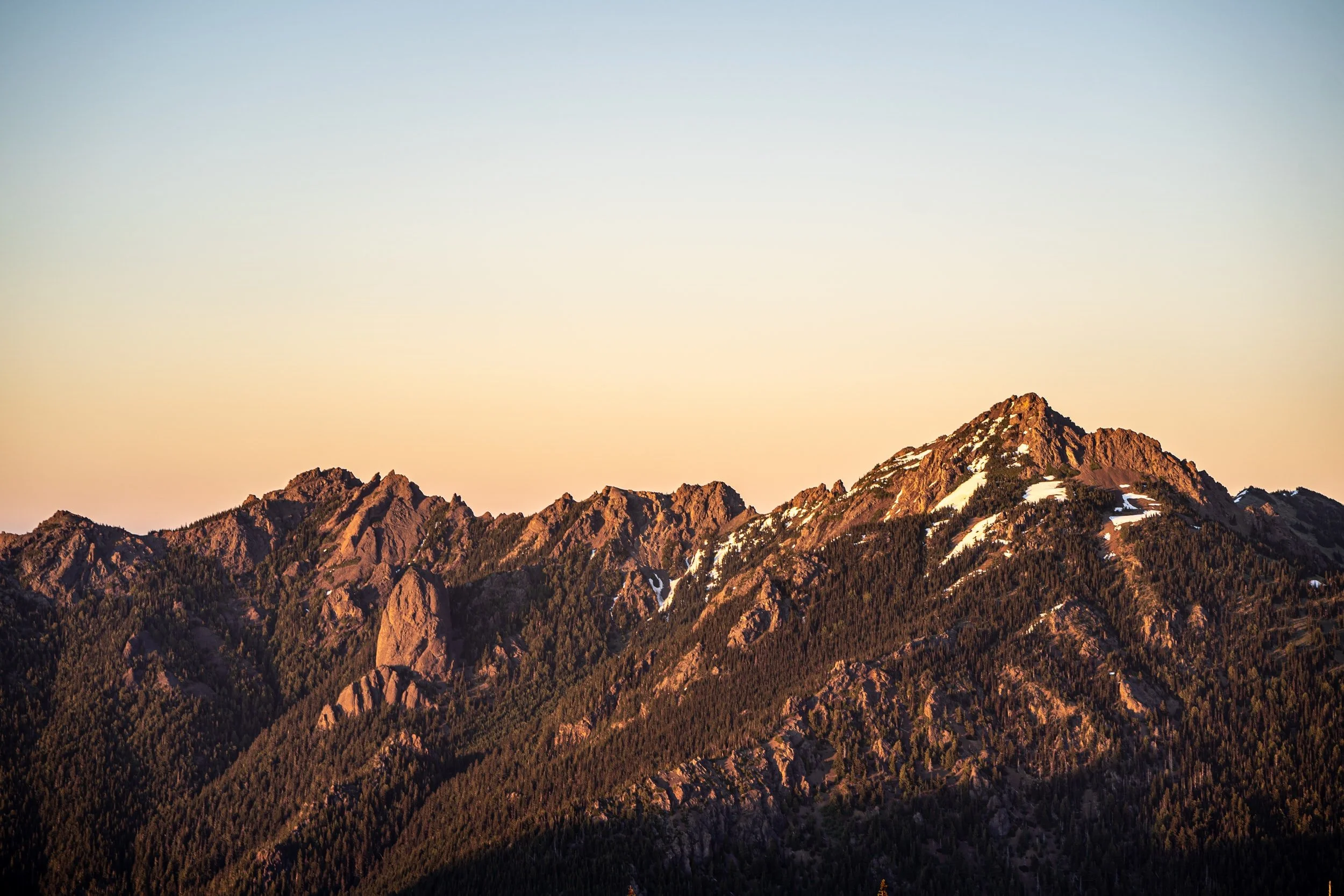 Snow-capped mountain peaks glowing at sunset with forested slopes