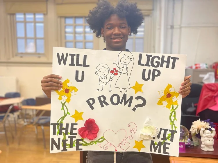 Student holding a handmade Will You Light Up Prom With Me sign