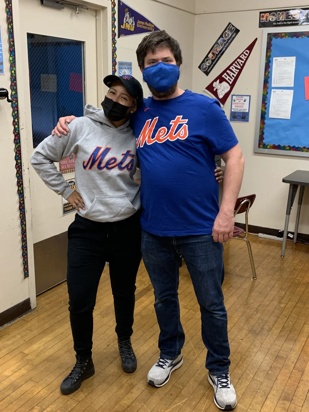 Two staff members wearing New York Mets gear in a classroom