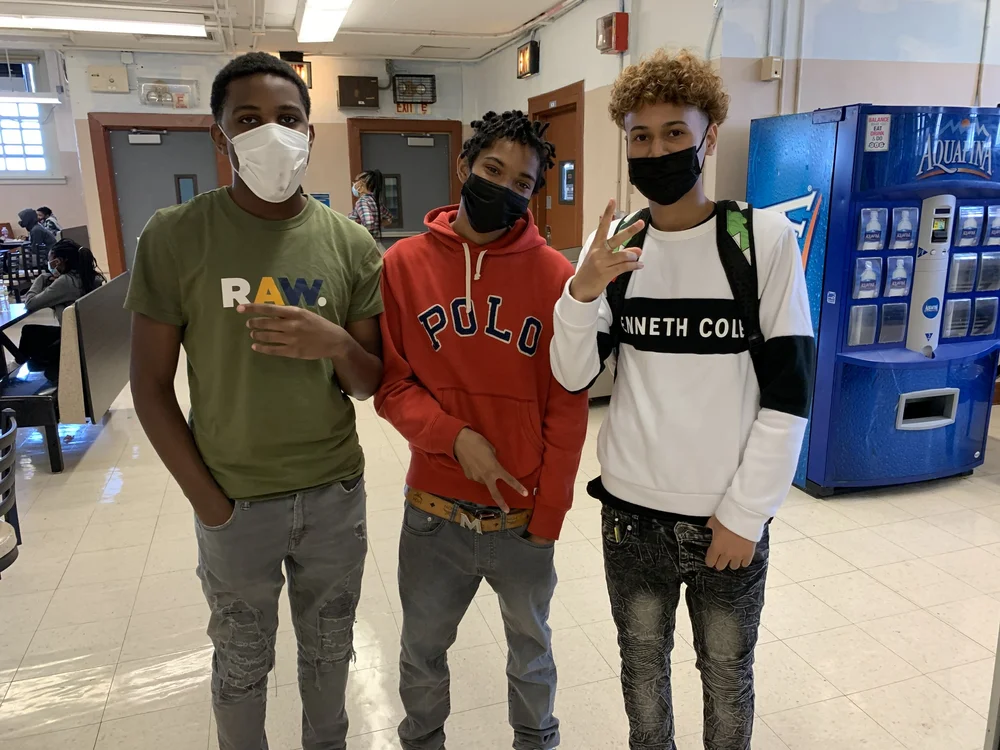 Three masked students posing together in school cafeteria