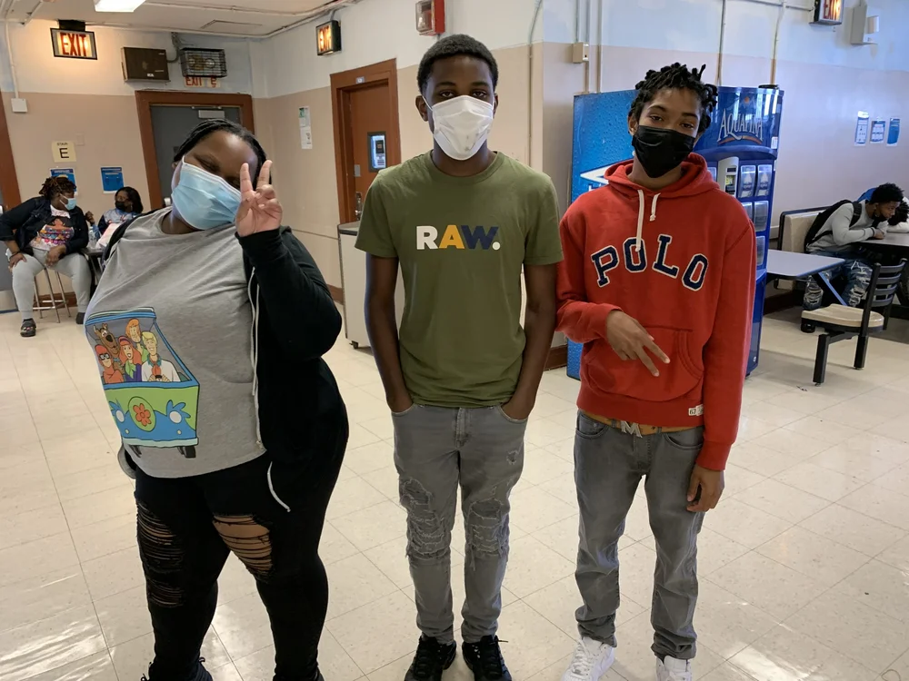Three masked students posing together in school cafeteria