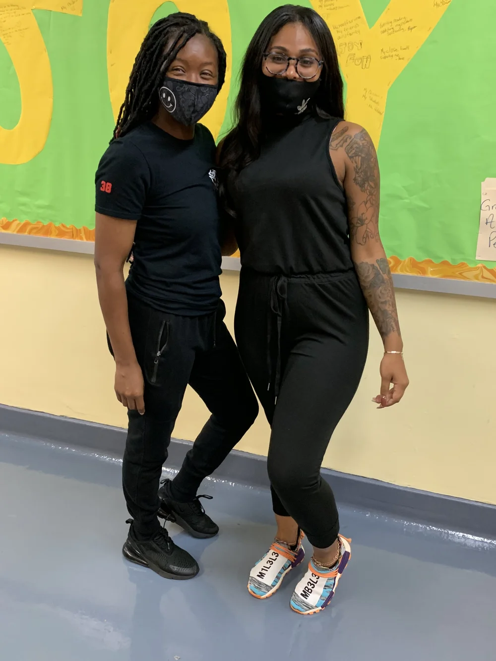 Two masked staff members posing together in a school hallway