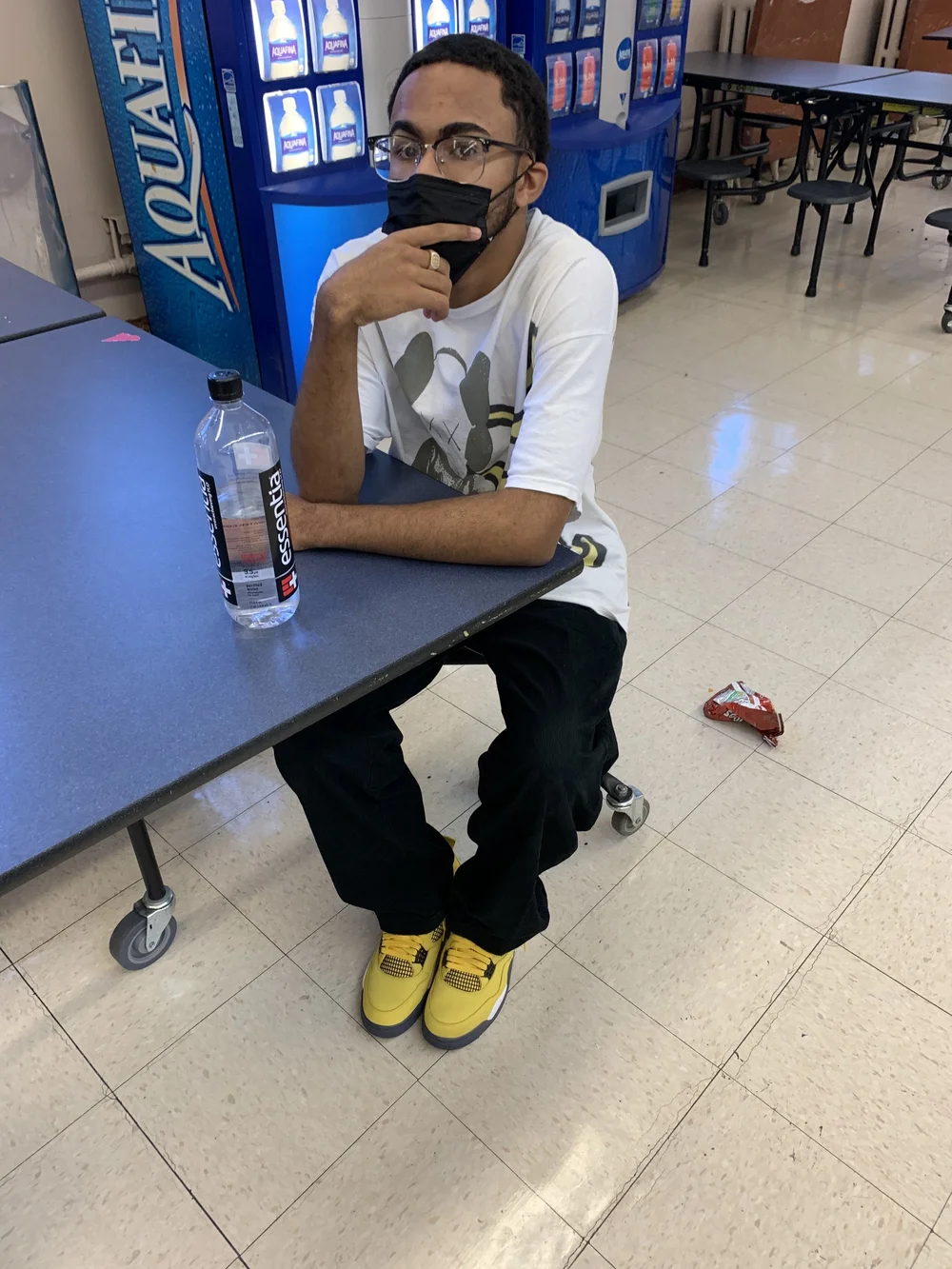 Student wearing a mask sitting alone in school cafeteria