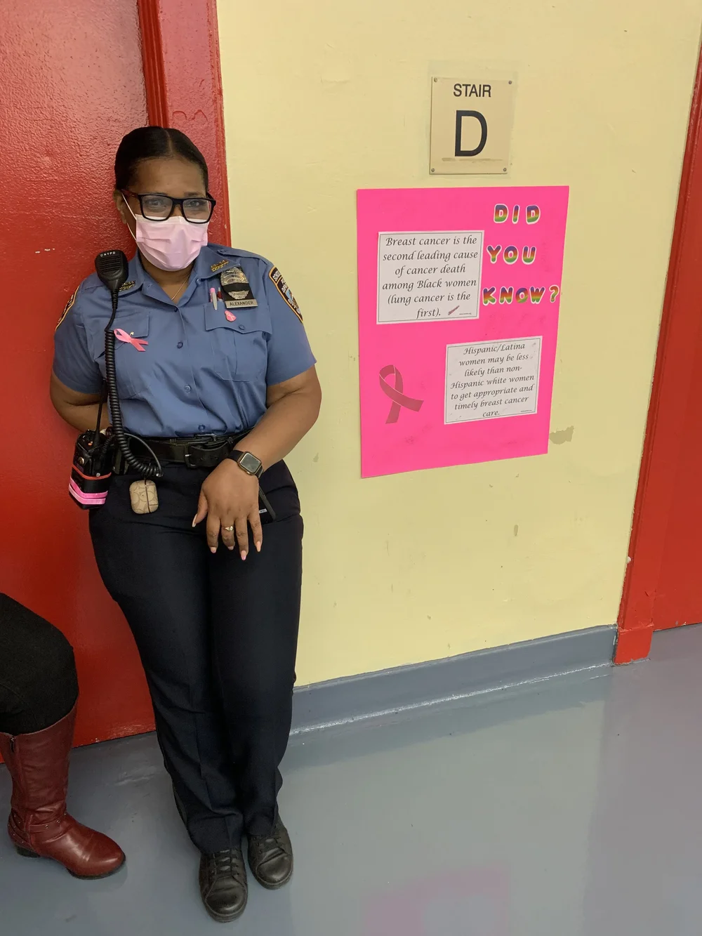 School safety agent beside breast cancer awareness poster in hallway