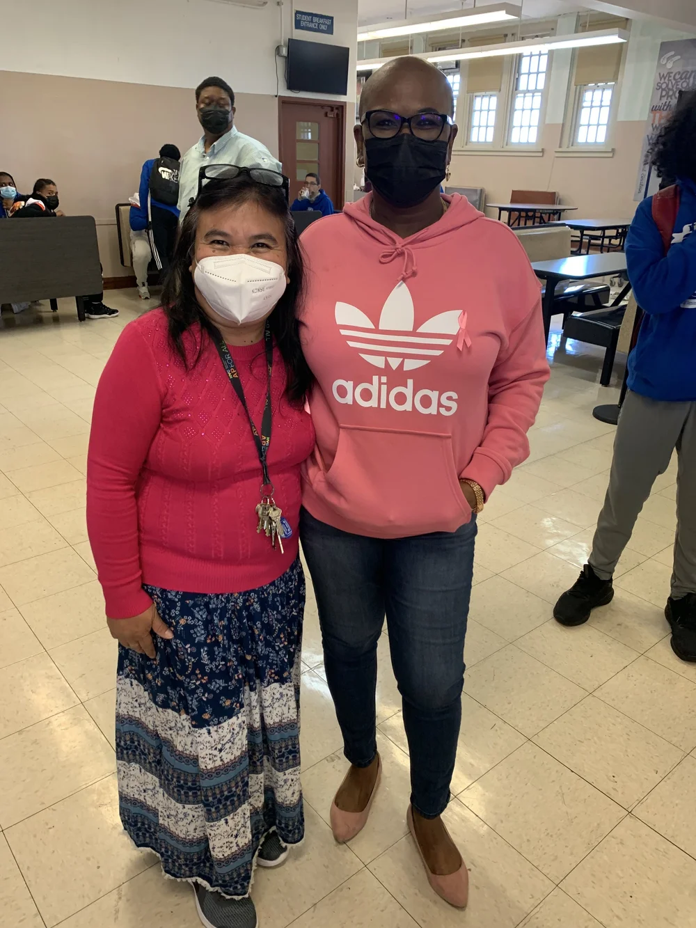 Two masked staff members posing together in school cafeteria