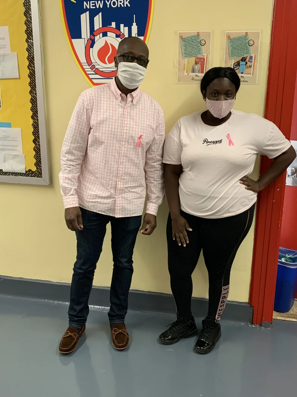 Two masked staff members wearing pink ribbons for breast cancer awareness